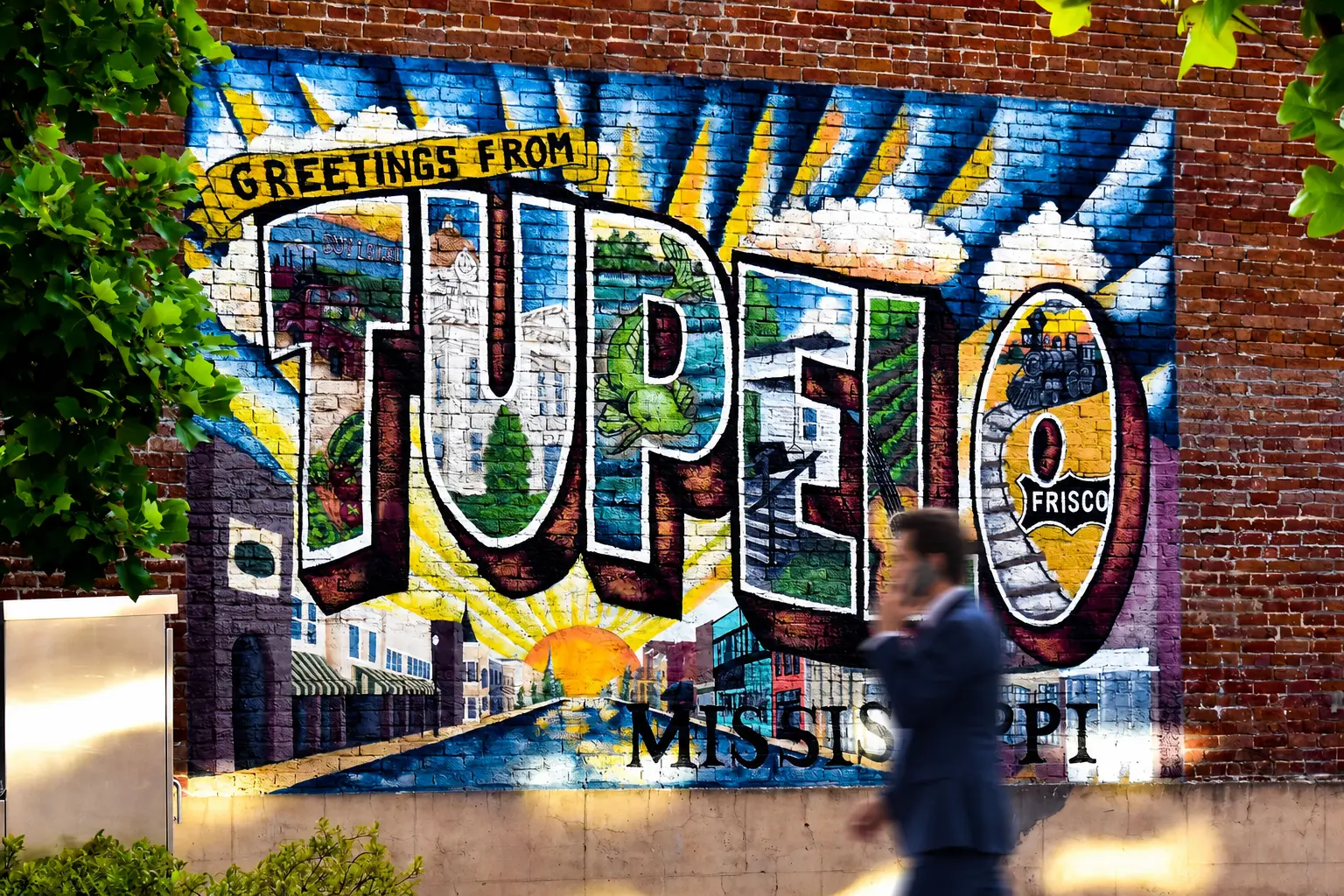 Attorney in a suit walking past the Greetings from Tupelo mural in downtown Tupelo, Mississippi